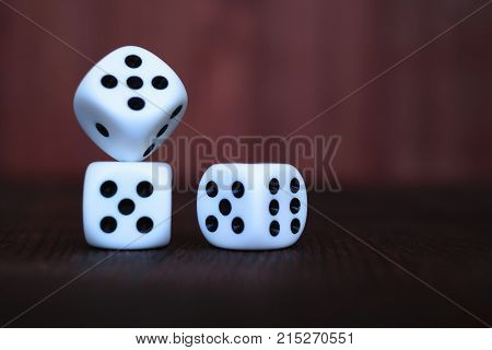 Heap of three white plastic dices on brown wooden board background. Six sides cube with black dots. Numbers 1 3 5 6.