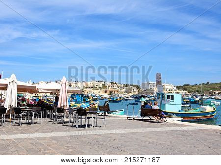 MARSAXLOKK, MALTA - APRIL 1, 2017 - Traditional Maltese Dghajsa fishing boats in the harbour with waterfront buildings to the rear and restaurants on the quayside Marsaxlokk Malta Europe, April 1, 2017.