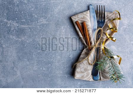 On the table, serve a fork and knife in a napkin and a Christmas tree branch. Against the background is a layout with a place for an inscription. View from above. Indoors.