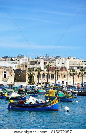 MARSAXLOKK, MALTA - APRIL 1, 2017 - Traditional Maltese Dghajsa fishing boats in the harbour with waterfront buildings to the rear Marsaxlokk Malta Europe, April 1, 2017.