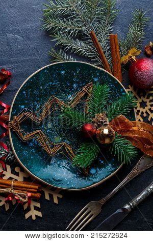 A decorative ornamental Christmas tree of branches is decorated with balls, a cone and ribbon on a beautiful round plate with a dark green glossy surface. View from above. Close-up. Indoors.