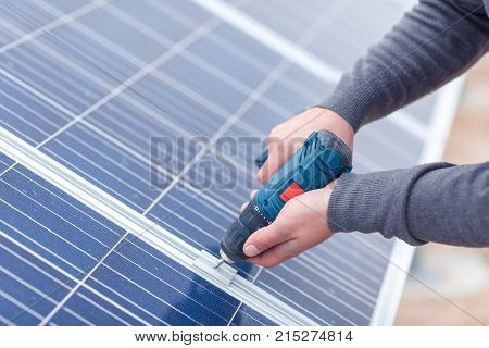 The hands of the solar battery station worker in the uniform drills the solar battery panel by the drill. Close-up. Outdoors.