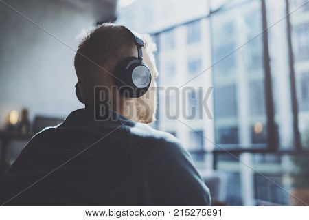 Attractive young man wearing glasses casual clothes.Man sitting in vintage armchair modern loft studio and relaxing whith headphone music. Blurred background.Horizontal