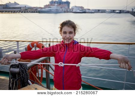 Girl in red jacket holds rope with three knots on ship deck.