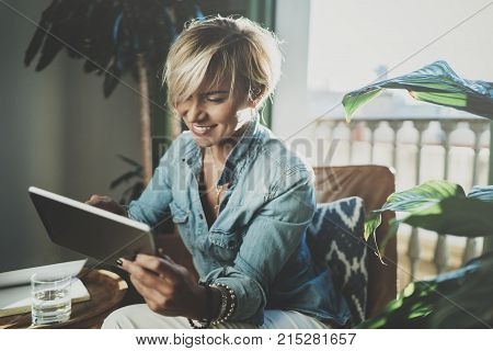 Smiling young woman wearing casual clothes and using electronic device while spending relax time in vacation travel.Attractive woman owner communicating on digital tablet.Blurred background
