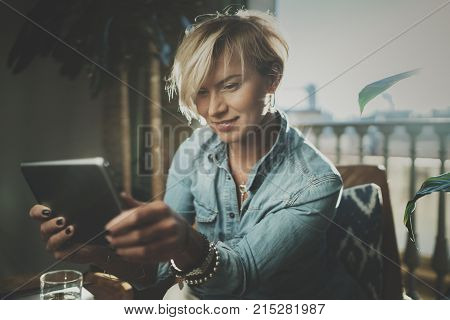 Smiling young woman wearing casual clothes and using electronic device while spending relax time in vacation travel.Attractive woman owner communicating on digital tablet.Blurred background