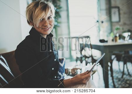 Smiling young woman wearing casual clothes and using electronic device while spending relax time in vacation travel.Attractive woman owner communicating on digital tablet.Blurred background