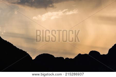 Sunlight of morning sky touching rain blowing by wind over dark scene of silhouetted mountain range at Samet Nangshe Phang Nga Thailand.