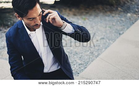 Businessman using contemporary smartphone taking rest outside the office during work day.Holding hands take away coffee cup.Blurred background. Horizontal.Cropped