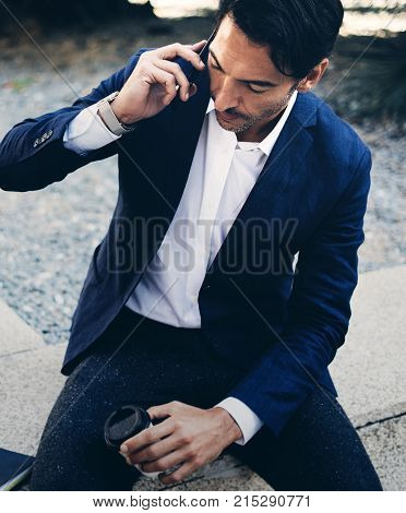 Businessman talking via modern smartphone while taking rest during work day.Holding hands take away coffee cup.Blurred background. Vertical