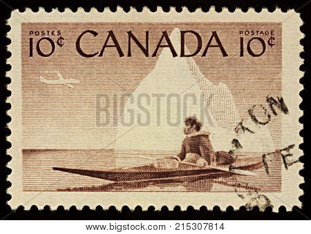 Moscow Russia - November 23 2017: A stamp printed in Canada shows Eskimo in a kayak on iceberg background series 