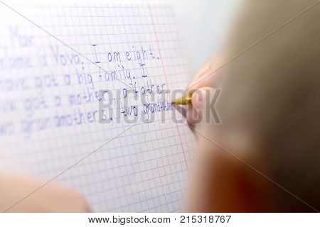 Close-up of boy hand with pencil writing english words by hand on traditional white notepad paper. Boy writes a letter to a friend