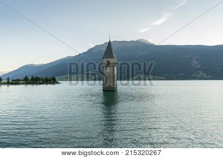 Church under water drowned village mountains landscape and peaks in background. Reschensee Lake Reschen Lago di Resia. Italy Europe Südtirol South Tyrol Upper Adige Alto Adige