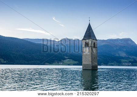 Church under water drowned village mountains landscape and peaks in background. Reschensee Lake Reschen Lago di Resia. Italy Europe Südtirol South Tyrol Upper Adige Alto Adige