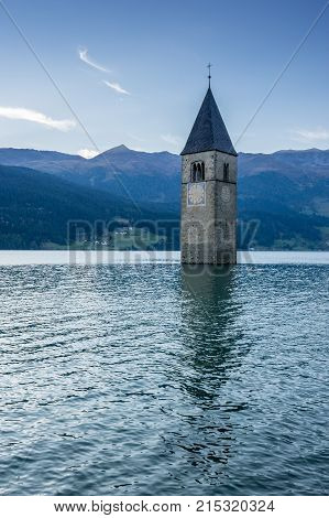 Church under water drowned village mountains landscape and peaks in background. Reschensee Lake Reschen Lago di Resia. Italy Europe Südtirol South Tyrol Upper Adige Alto Adige