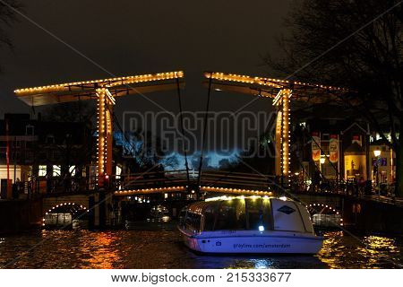 Amsterdam, Netherlands - January 14, 2017: Illuminated drawbridge by night in Amsterdam seen from the water