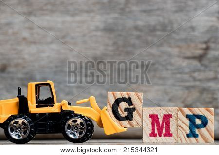 Yellow plastic bulldozer hold letter G to complete word GMP (Abbreviation of Good Manufacturinc Practice) on wood background