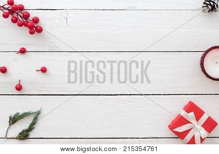 Christmas background with red gift box holly berry fir leaves pine cone and candle on white wooden background. Creative Flat layout and top view design.