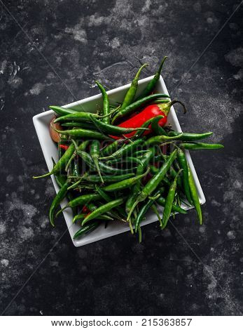 Green, red chili Peppers in white bowl on black background.