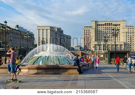 MOSCOW RUSSIA - JULY 23 2016: Unknown people rest on Manezhnaya square. Four Seasons Hotel Moscow 5* (formerly - Moscow Hotel) and building of State Duma