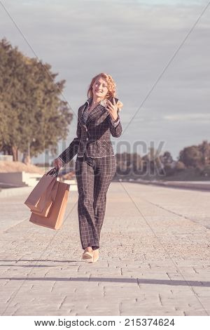 Vertical orange tonted shot of a happy beautiful blond woman with braces running with paper bags and phone in hand along the promenade