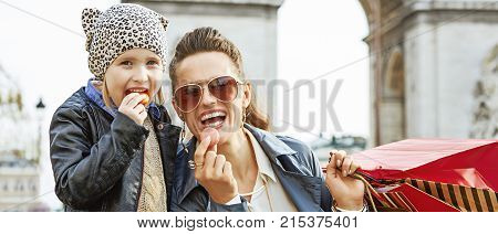Stylish autumn in Paris. Portrait of smiling modern mother and daughter with shopping bags near Arc de Triomphe in Paris France eating macaroons