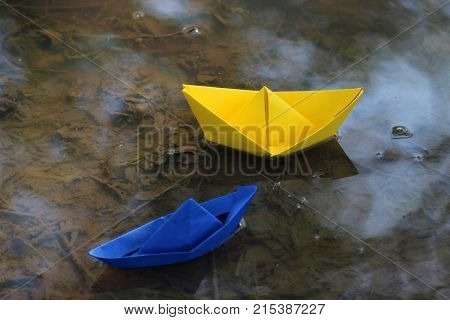 a yellow and a blue paperboat swimming in a puddle