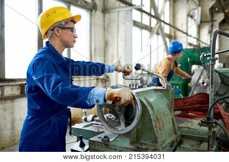 Concentrated confident engineer working on tailstock and rolling wheel in factory workshop