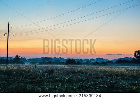 Power lines in misty sunrise over firld, copy space
