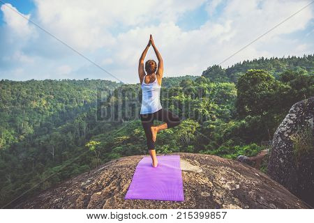 Asian women relax in the holiday. Play if yoga. On the Moutain rock cliff. Nature of mountain forests in Thailand