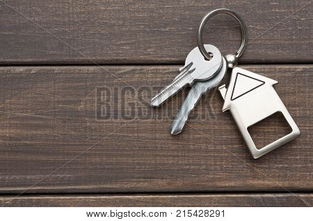 Two steel keys with house shaped trinklet on keyring on brown rustic wooden background with copy space. Home key, safety, security, real estate and rent concept, top view