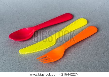 a set of colorful plastic Cultery: spoon fork knife on gray background.