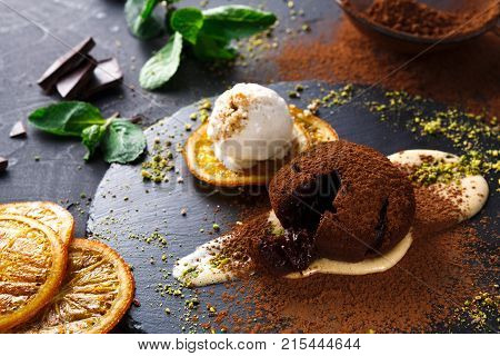 Exquisite french dessert. Chocolate fondant with creme anglaise and vanilla ice cream, sprinkled with cocoa powder, served on round slate decorated with orange citron and pistachio crumble, closeup
