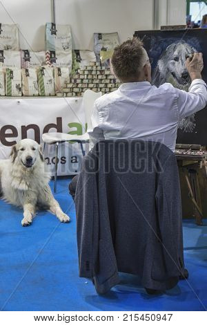 MALAGASPAIN-NOVEMBER 25:We see in the image a painter making a portrait of a dog that is lying in front of him. They are in a meals for dogs stand.On November 25 2017 in Malaga Spain.