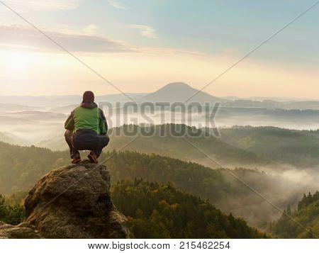 Man Stay On Rocky Peak Within Daybreak And Watch Over Misty Landscape.