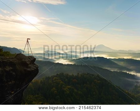 Tripod  With Camera On View Point Ready For Photography. Exposed Rocky Edge Above Landscape.