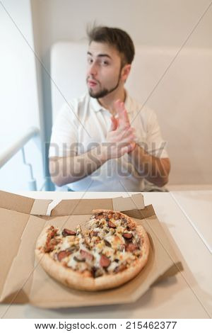 Man sitting at a table near the pizza box looking at the camera. Focus on pizza. Pizza on the background of a man