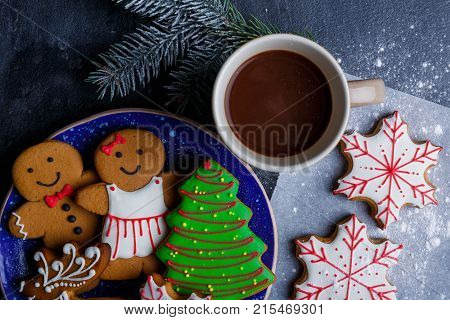 Close-up is the Christmas composition, with different shapes of cookies in a plate, coffee in a cup, a sprig of spruce, and it's all on a black background.