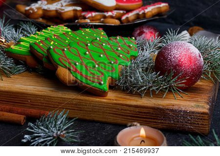 Close-up on a wooden board is a green Christmas tree shaped biscuit, a red toy ball, a spruce sprig, a candle burns, a New Year's concept, a new year, Christmas.