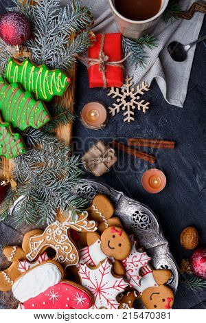 New Year concept, top view, on the table New Year's cookies of different shapes, cinnamon sticks, coffee, gift boxes, round small candles, snowflake, all this on a black background.