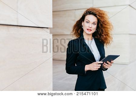 Beautiful Businesswoman With Curly Fluffy Hair, Wearing Elegant Clothes, Holding Tablet In Hands, Wa