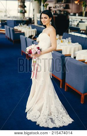 Portrait Of Pretty Female Bride Dressed In Wonderful White Wedding Dress, Holds Beautiful Bouquete,