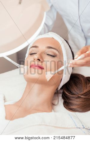 High-angle close-up view of the face of a beautiful woman during anti-aging facial massage with soft brushes in a modern cosmetic center