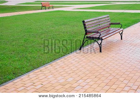 Wooden park bench at a park. Walkway and lawn.