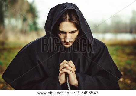 a monk in a black robe praying in the woods on his knees