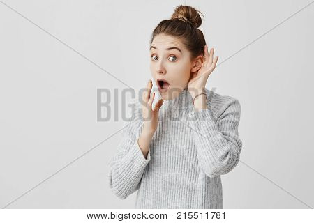 Woman with hair in bun listening to something holding hand near her ear. Curious girl being attentive trying to overhear some news. Curiosity concept