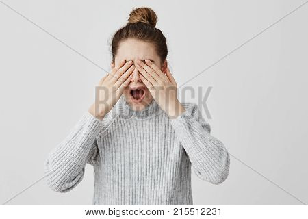 Brunette female screaming in fright covering eyes with hands. Young woman feeling fear doesn't want to see what happened. Terror, emotions concept