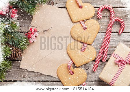 Christmas heart gingerbread cookies, candy canes and snow fir tree on wooden table. Top view with piece of paper for your greetings