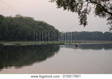 Wide river flowing across green forest. Fall. Evening. Reflections of trees in the calm water. Sundown