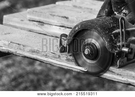 male hands with circular saw while workimg with wood in black and white.